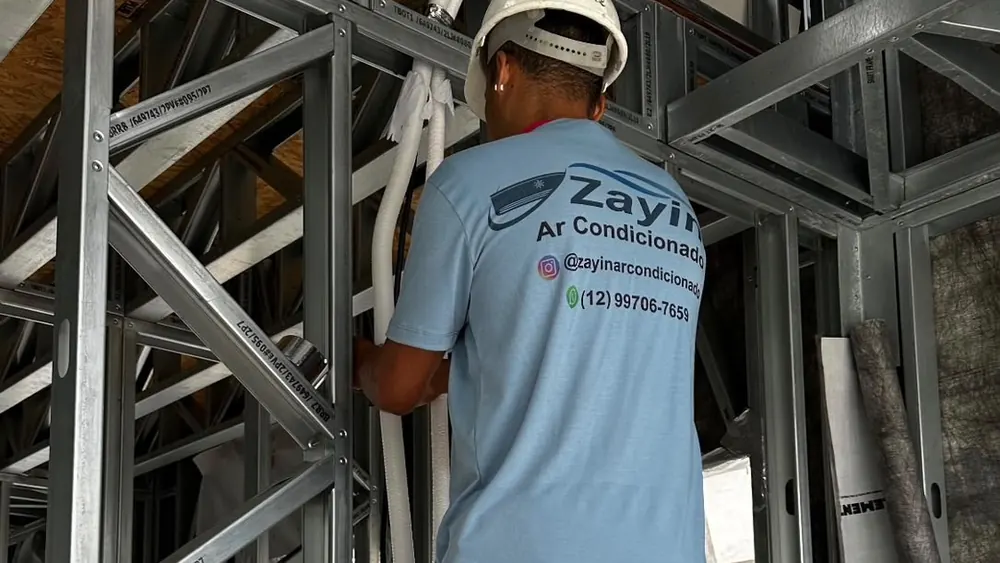 Técnico da Zayin passando a tubulação do ar-condicionado pela estrutura de uma obra